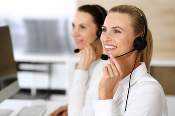 Call center. Happy and excited business woman using headset while consulting clients online. Customer service office or telemarketing department. Smiling group of operators at work