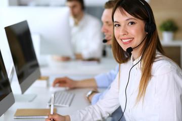 Call center. Group of diverse operators at work. Focus on beautiful asian woman in headset at customer service office. Business concept