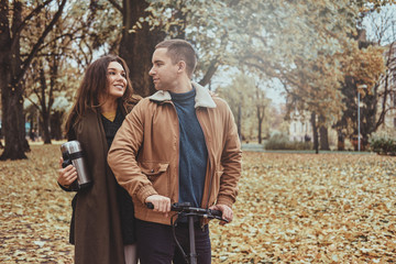 Attractive couple has a nice romantic walk at autumn park with scooter.
