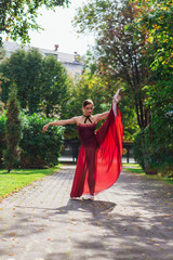 Woman ballerina in red ballet dress dancing in pointe shoes in autumn park.