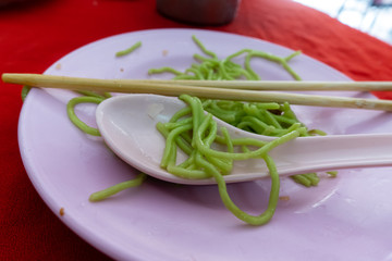 Green noodles on plastic plates and wooden chopsticks