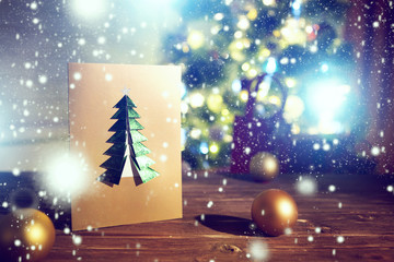 Handmade christmas paper postcard on wooden table over christmas tree and lights