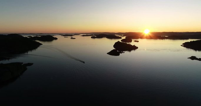 Aerial view of small boat crossing paceful water during sunset over norwegian archipelago.