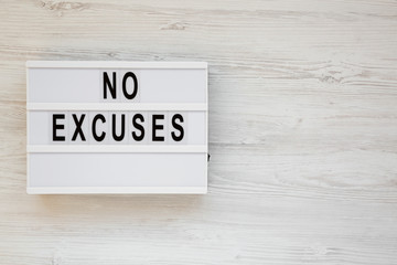 'No excuses' words on a lightbox on a white wooden background, top view. Overhead, from above, flat lay. Copy space.