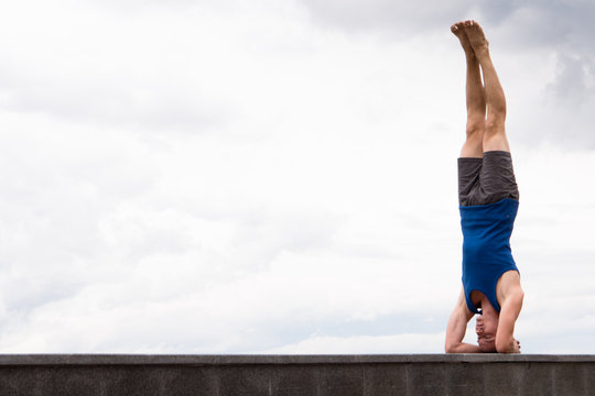 young man in shirshasana doing yoga on sky background