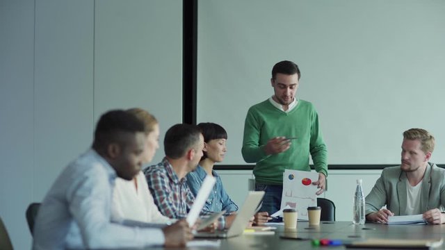 Tracking shot of diverse business team discussing financial results in meeting. Man presenting document with statistical charts to colleagues in board room