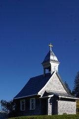 Wunderschöne kleine Kirche mit einem  goldenen Kreuz in den Alpen vor strahlend blauem Himmel