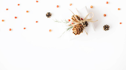 Christmas composition of natural materials. Christmas gift wrapped in craft paper, knitted blanket, pine cones, fir branches on white background. Flat lay, top view, with copy space.