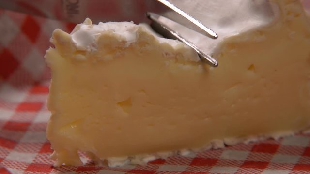 Piece of soft appetizing camambert cheese is cut with a fork on the background of a red and white vichy napkin vichy