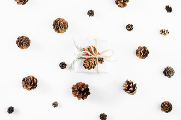 Christmas composition of natural materials. Christmas gift wrapped in craft paper, knitted blanket, pine cones, fir branches on white background. Flat lay, top view, with copy space.