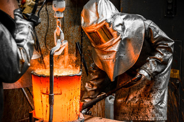In a foundry workshop. Workers protected by their safety equipment handle a crucible containing...