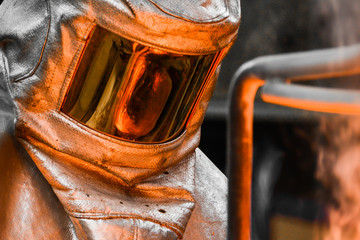 In a foundry workshop. The molten metal contained in a crucible is reflected on the visor of a...