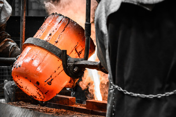 In a foundry workshop. The molten metal is poured into a mold from a crucible maneuvered by two...