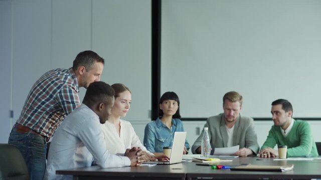 Tracking shot of diverse business people planning project in meeting room. Part of business team looking at presentation on laptop screen, their colleagues reading document