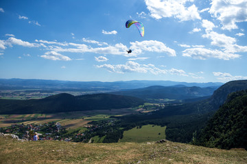 A colorful paraglider flying high in the sky above Hohe Wand. Above are beautiful clouds in the...