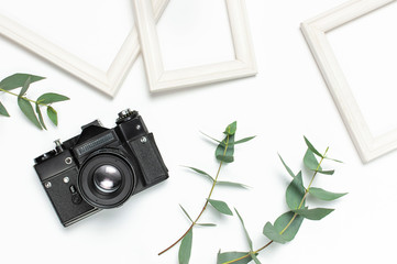 White photo frame, old retro photo camera and green eucalyptus leaves on white background. Flat lay...