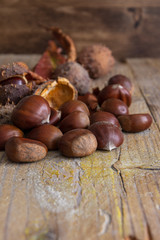Top view of still life of chestnuts, with its spiny wrap and unfocused brown leaves, on weathered wooden background in vertical
