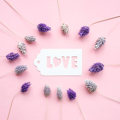White gift tag with inscription love, on a pink background, decorated with dried flowers of gently purple color.