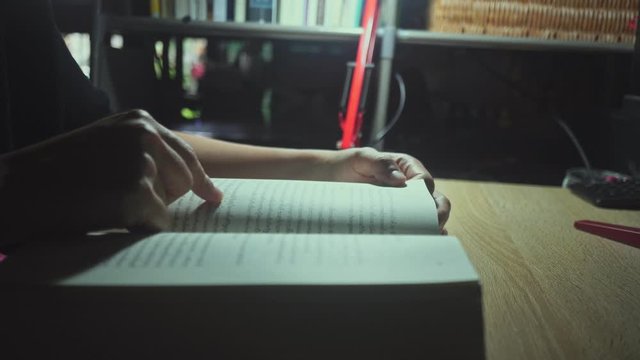 4K video woman is focus to read book on dest with light from lamp in dark room.