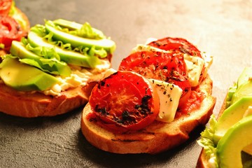 Bruschetta on a dark table background. Bruschetta with grilled  tomatoes, mozzarella and avocado. Delicious vegetarian healthy sandwiches. Tasty snack.