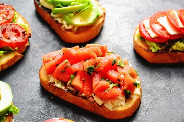 Bruschetta on a dark table background. Bruschetta with grilled  tomatoes, mozzarella and avocado. Delicious vegetarian healthy sandwiches. Tasty snack.