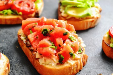 Bruschetta on a dark table background. Bruschetta with grilled  tomatoes, mozzarella and avocado. Delicious vegetarian healthy sandwiches. Tasty snack.