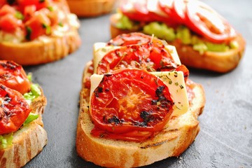 Bruschetta on a dark table background. Bruschetta with tomatoes, mozzarella and avocado. Delicious vegetarian healthy sandwiches. Tasty snack on the pink plate.