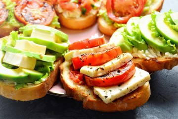 Bruschetta on a dark table background. Bruschetta with tomatoes, mozzarella and avocado. Delicious vegetarian healthy sandwiches. Tasty snack on the pink plate.