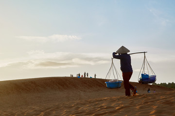 Fototapeta premium A man carries a load across the desert at sunset
