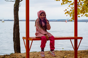little girl, autumn in the cold sitting on a Park bench, focus in the foreground