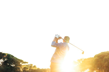 Male golf player teeing off golf ball from tee box to beautiful sunset