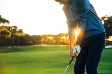 Poster Male golf player teeing off golf ball from tee box to beautiful sunset © karrastock