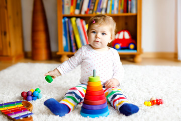 Adorable cute beautiful little baby girl playing with educational toys at home or nursery. Happy healthy child having fun with colorful wooden rainboy toy pyramid. Kid learning different skills
