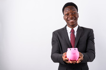 Young handsome African businessman holding piggy bank against wh