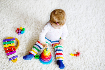 Adorable cute beautiful little baby girl playing with educational toys at home or nursery. Happy healthy child having fun with colorful wooden rainboy toy pyramid. Kid learning different skills