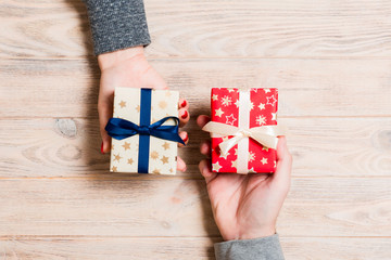 Top view of a woman and a man exchanging gifts on wooden background. Couple give presents to each other. Close up of making surprise for holiday concept