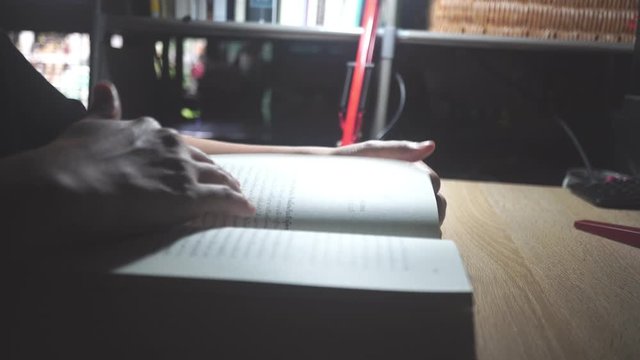 4K video woman is focus to read book on dest with light from lamp in dark room.