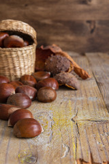 Top view of still life of chestnuts with dried leaves and unfocused wrappers, on weathered wooden background in vertical