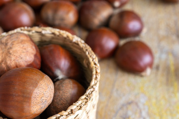 Top view of chestnuts in a basket, with unfocused chestnuts on weathered wooden background horizontal