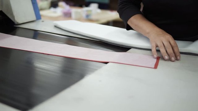 Close up footage of woman's hands - unidentified garment factory worker places pieces of textile, fabric pattern piece for gluing it inside the iron, drag machine, conveyor. Slow motion