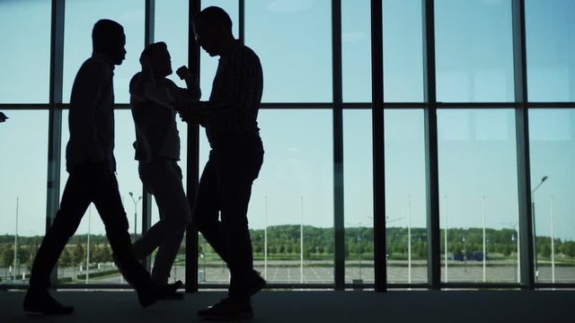 Silhouettes of serious business people with documents and notepads walking in office lobby while funny carefree man walking in dance near panoramic window in slow motion