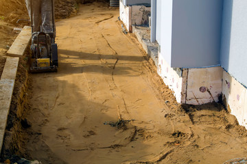 worker compresses sand in blind area around building with special working tool (tamping machine or...