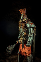 Powerful knight in the armor with the hammer. Dungeon on the background.
