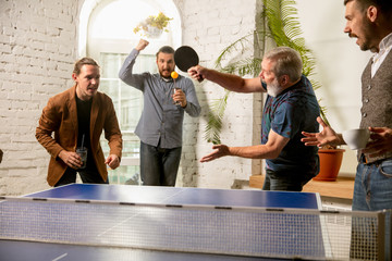 Young people playing table tennis in workplace, having fun. Friends in casual clothes play ping...