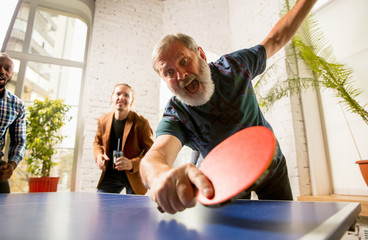 Young people playing table tennis in workplace, having fun. Friends in casual clothes play ping...