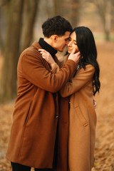 Stylish young couple outdoors on a beautiful autumn day in the forest. Young couple in love holding hands and walking through a park on a  autumn day. The concept of youth, love and lifestyle.