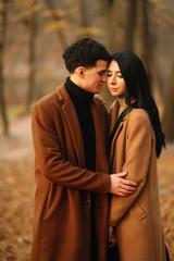 Stylish young couple outdoors on a beautiful autumn day in the forest. Young couple in love holding hands and walking through a park on a  autumn day. The concept of youth, love and lifestyle.