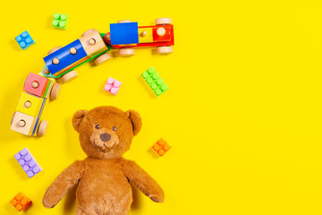 Baby kids toys background. Teddy bear, wooden train and colorful blocks on yellow background