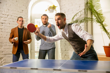 Young people playing table tennis in workplace, having fun. Friends in casual clothes play ping...