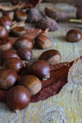 Close-up of chestnuts with leaves and wrappers with unfocused skewers, on weathered wooden background in vertical